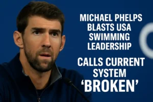 Michael Phelps in a serious close-up at a press event, wearing a navy sports jacket, with bold white text beside him reading “Michael Phelps Blasts USA Swimming Leadership — Calls Current System ‘Broken’.”Michael Phelps First-Day Firestorm