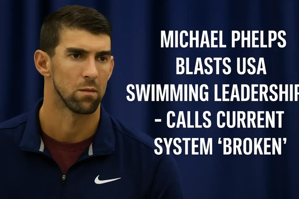 Michael Phelps wearing a navy Nike jacket over a maroon T-shirt, standing in front of a blurred blue curtain, with bold white text beside him reading “Michael Phelps Blasts USA Swimming Leadership – Calls Current System ‘Broken’.”